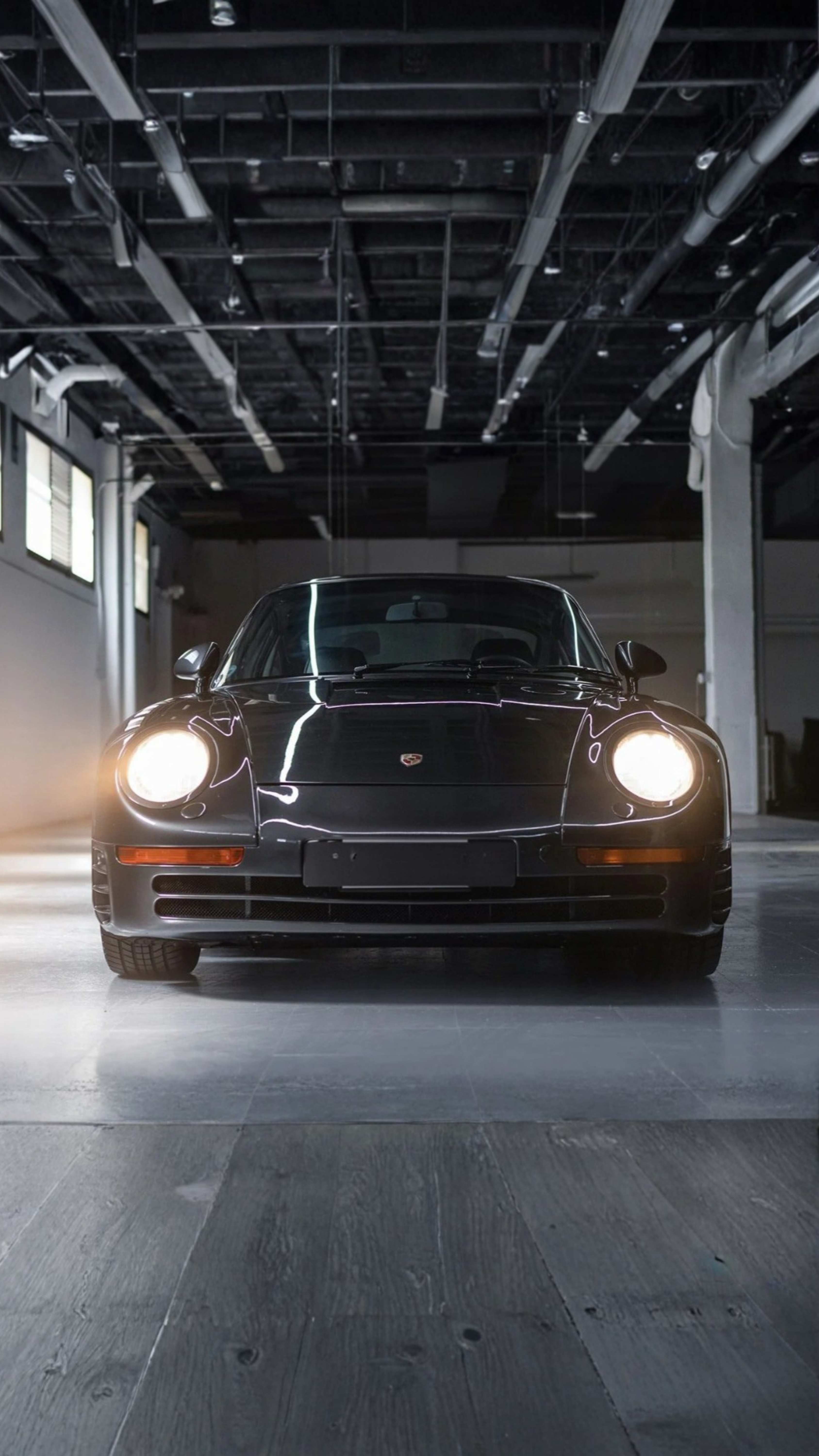 Black Porsche parked in an industrial warehouse with headlights on
